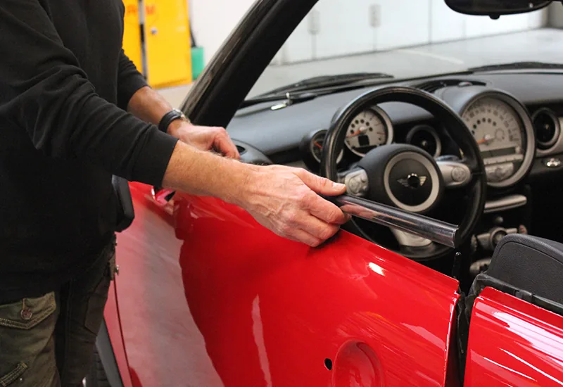 Vakman werkt aan het ruitrubber van een rode cabriolet in de werkplaats