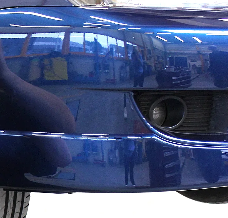 Hoogglans donkerblauwe bumper na herstel, met de werkplaats erin weerspiegeld